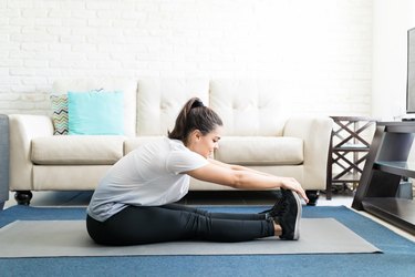 Person in white T-shirt and black leggings doing stretching workout at home
