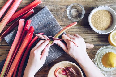 Hands slicing rhubarb stalks with other ingredients on side