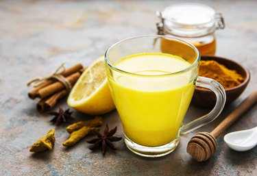 Yellow turmeric latte drink. Golden milk with cinnamon, turmeric, ginger  and honey over concrete background.