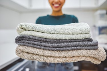 a smiling person holding a stack of fresh, clean towels