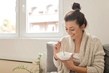 Woman at home eating a bowl of oatmeal to help her poop better