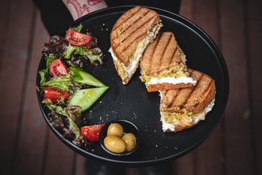 Toasted Sandwich with side salad and small bowl of olives on black plate