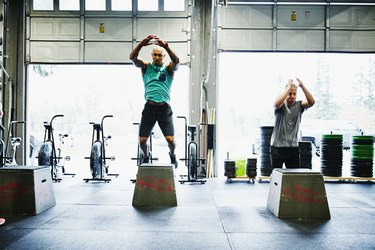 Two people in gym performing box jumps demonstrating how to pace yourself during a HIIT workout.