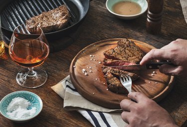 Man is eating grilled steak at wooden table