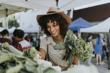 A woman at a farmers' market holds a bunch of kale