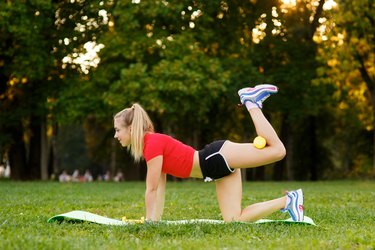 Healthy young sportswoman doing the donkey kick exercise on all fours arching back straightening leg up outdoors. Concept sport, fitness, lifestyle