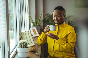 Black woman drinking coffee and looking out window at home wondering is bupropion a stimulant