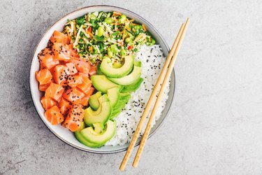 Poke bowl with healthy fats like salmon and avocado served white bowl on gray countertop.