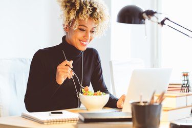 Young woman eating a salad for lunch at her desk while working.