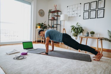 man wearing a blue t-shirt and black joggers doing push-ups and shoulder exercises at home