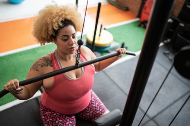 Young Black person assigned female at birth in red tank top pulling weight machine at the gym wondering how much is 8 ounces of water in a water bottle for soccer players