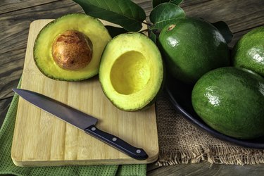 Close up of green ripe avocados with leaves on cutting board with knife