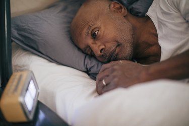 a bald person in a white t-shirt lying awake in bed, wondering how to improve sleep latency