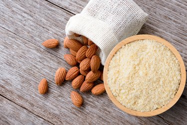 Almond powder in wooden bowl and almonds nut isolated on wooden table background.
