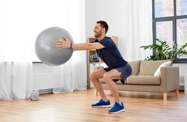 man exercising and doing squats with ball at home