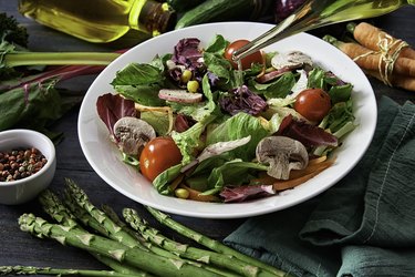 drizzling olive oil on a spring salad shot from above on rustic wood table to convey eating healthier or starting a diet