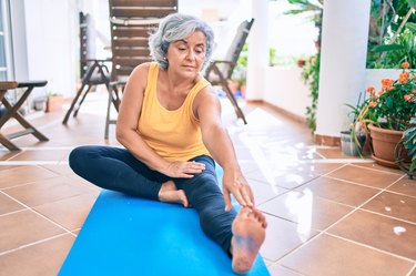 Older woman stretching on yoga mat.