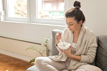Woman eating a bowl of oatmeal at home on her couch