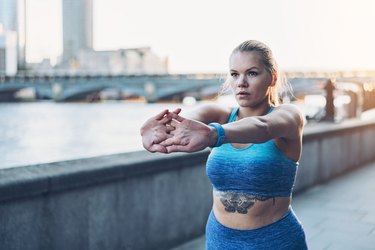 Person in a blue sports bra and blue leggings stretching before a run in the city, as a way to firm up sagging breasts