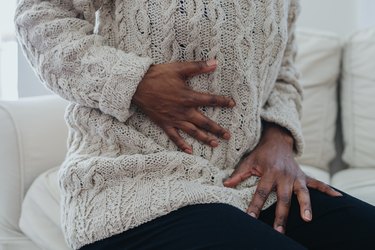 Close up view of a person wearing a beige sweater holding his abdomen after being diagnosed with post-infectious irritable bowel syndrome