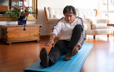 Older adult with short dark hair exercising at home and trying to stretch their legs