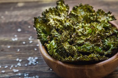 Homemade green kale chips baked with balsamic vinegar in bowl on rustic wooden background