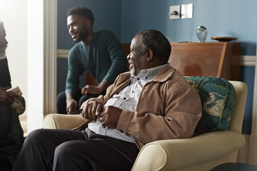 Senior man sitting down looking at friends talking at home