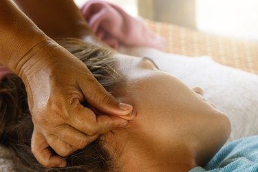 Cropped hand of a massage therapist placing magnetic weight loss earrings on a person's head