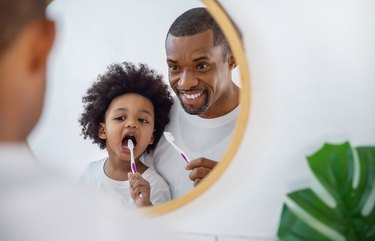 Portrait of happy family black African American father and son child boy brushing teeth in the bathroom. Morning routine with toothbrushes, fatherâs day concept