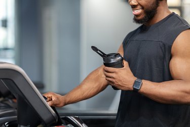 Close view of muscular man on treadmill holding bottle of krealkyline true athlete creatine shake