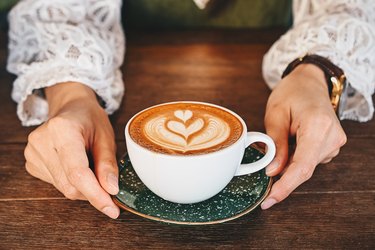 overhead shot of a woman's hands holding a cup of hot latte coffee on wooden table