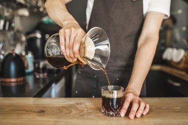 Barista's hand pouring freshly brewed coffee into glass, which may cause blurry vision, blurred vision and shaking hands