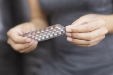 close up of hands holding pack of white and pink birth control pills for PCOS treatment
