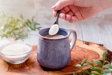 Woman's hand adding collagen powder supplement to her morning coffee.