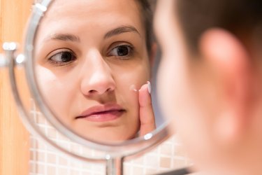 Young girl in front of a bathroom mirror putting baking soda on a pimple, as a home remedy for acne