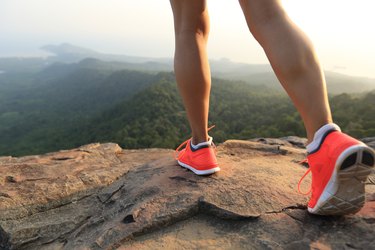 closeup of a young healthy woman's calves and shoes as she stands on a mountain peak rock