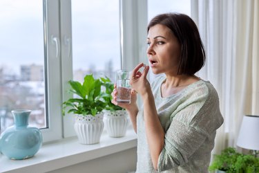 中年妇女维生素和一杯水在她的手,在冬天在家里