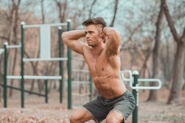 Man squatting while holding hands behind head