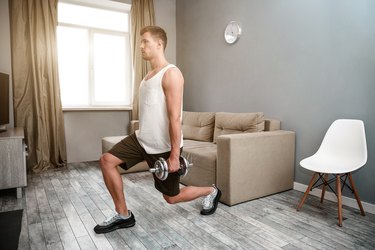 side view of a caucasian man doing a split squat, one of the best exercises for men to  get lean, in his living room