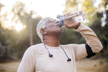 a person wearing a long sleeve shirt, headphones and a running armband drinks cold water for cold on the stomach