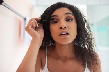 woman putting on mascara in her bathroom at home