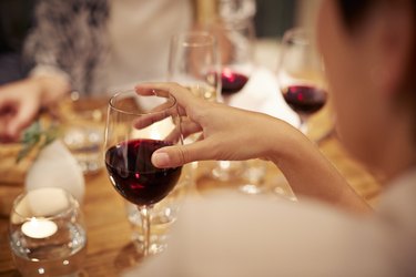 Over-the-shoulder view of a person holding a glass of red wine, one of the diverticulitis drinks to avoid