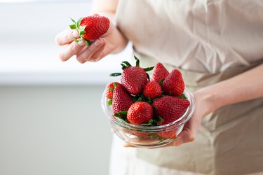 close view of a person holding a glass bowl of ripe red strawberries, as an example of foods to ease constipation