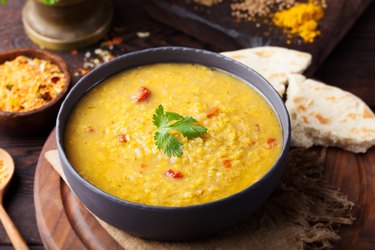 Red lentil Indian soup in a black bowl with flat bread on the side