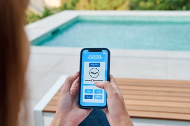 Woman using an application on her smartphone to control the water temperature of her swimming pool.
