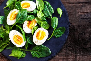 Fresh green spinach leaves and boiled eggs cut in a half on wooden background