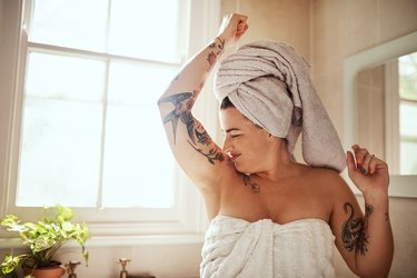A woman in a bath towel smelling her armpits