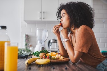 a woman sitting at her kitchen island eating fruit, as a home remedy for kidney stones