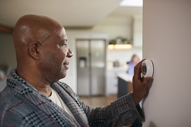 Mature man in pajamas turning down the thermostat before bed