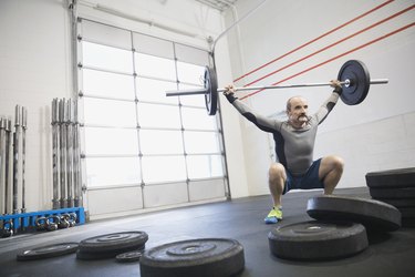 Older adult lifting barbell at gym as exercise for testicles